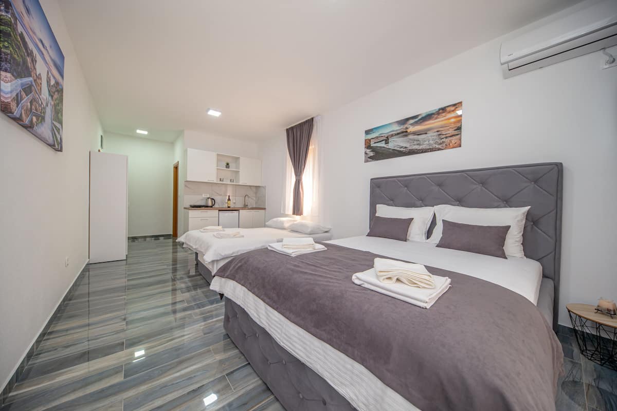 A hotel room with a large bed, a smaller bed, a kitchenette, and a bathroom.