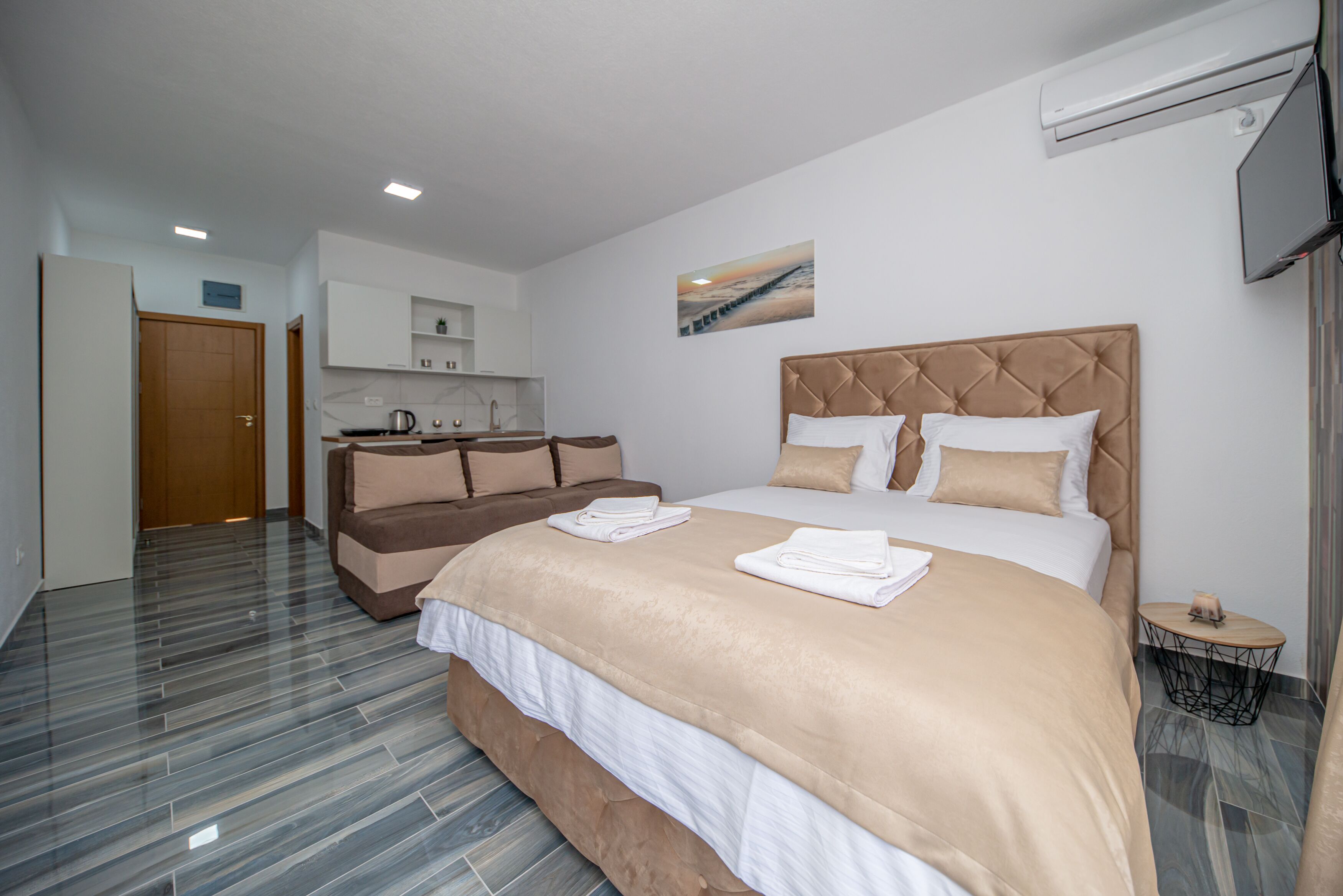 Habitación de hotel con una cama grande, un sofá cama, una zona de cocina y un televisor.