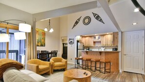 A modern living room with a sofa, armchairs, and a coffee table. A kitchen with wooden cabinets and bar stools is visible in the background. - Wild Irishman Off-Piste Condo: Great Keystone Getaway (Keystone)