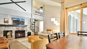 A modern living room with a stone fireplace, a spiral staircase, a sofa, and a dining table. - Wild Irishman Off-Piste Condo: Great Keystone Getaway (Keystone)