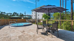 Un jardín trasero con un jacuzzi, mobiliario de patio y un gran paraguas.