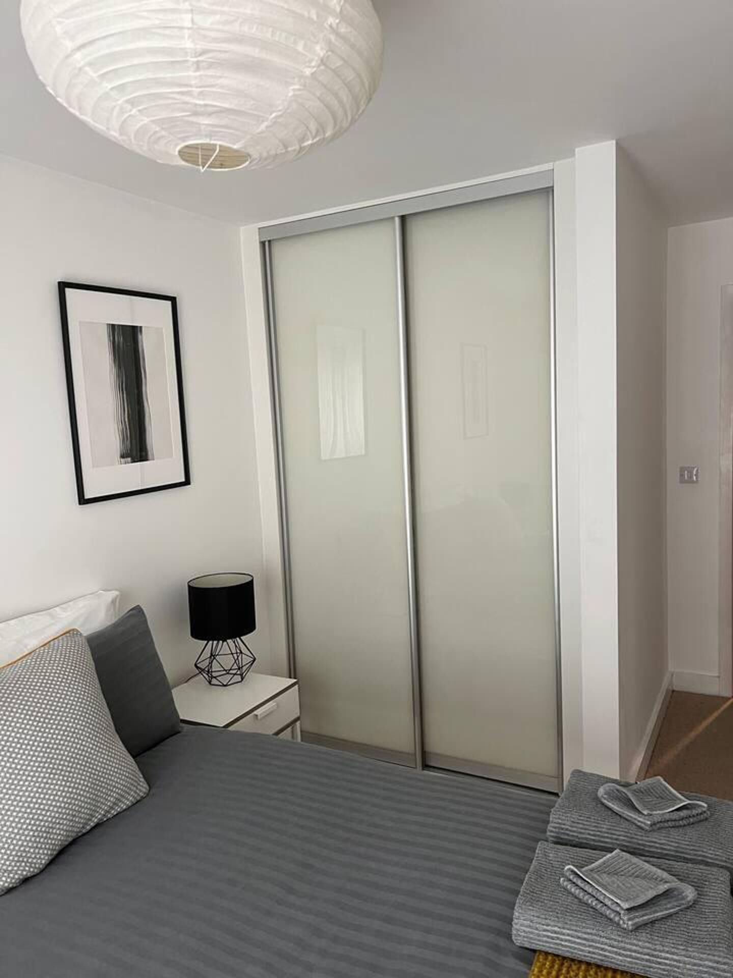 Une chambre à coucher avec un lit, une table de chevet avec une lampe, une armoire et un tableau encadré au mur.