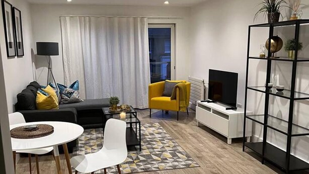 Una sala de estar moderna con un sofá, un sillón amarillo, un televisor y una estantería.