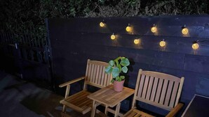 A wooden outdoor seating area with a table and chairs, a potted plant, and string lights. - Modern and Spacious 2 Bedroom Flat Near Shoreditch (London)