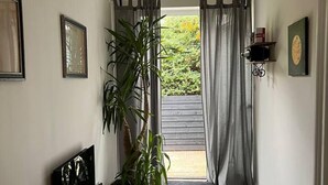 A hallway with a dark wooden floor, a potted plant, a hanging light fixture, and a door leading outside. - Modern and Spacious 2 Bedroom Flat Near Shoreditch (London)