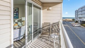 A balcony with a sliding glass door, outdoor seating, and a view of the street and ocean.