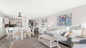 A modern living room with a grey sofa, a coffee table, and a dining area with white furniture.