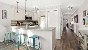 A modern kitchen with white cabinets, a central island with stools, and pendant lighting.