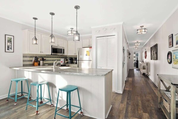 A modern kitchen with white cabinets, a central island with stools, and pendant lighting.