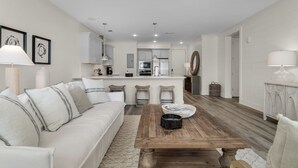 Een moderne woonkamer met een bank, salontafel en een keuken op de achtergrond.