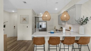 Une cuisine moderne dotée d’un îlot central, de luminaires suspendus et de tabourets de bar.