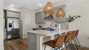 A modern kitchen with a stainless steel refrigerator, a white island with bar stools, and pendant lighting. - Enjoy a Romantic Getaway w/ 1 BR Cozy Condo on 30A + Free Attraction Tickets! (Santa Rosa Beach)