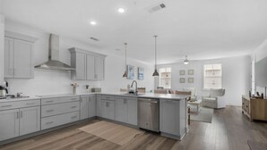 Une cuisine moderne avec des meubles gris, un lave-vaisselle et des luminaires suspendus.