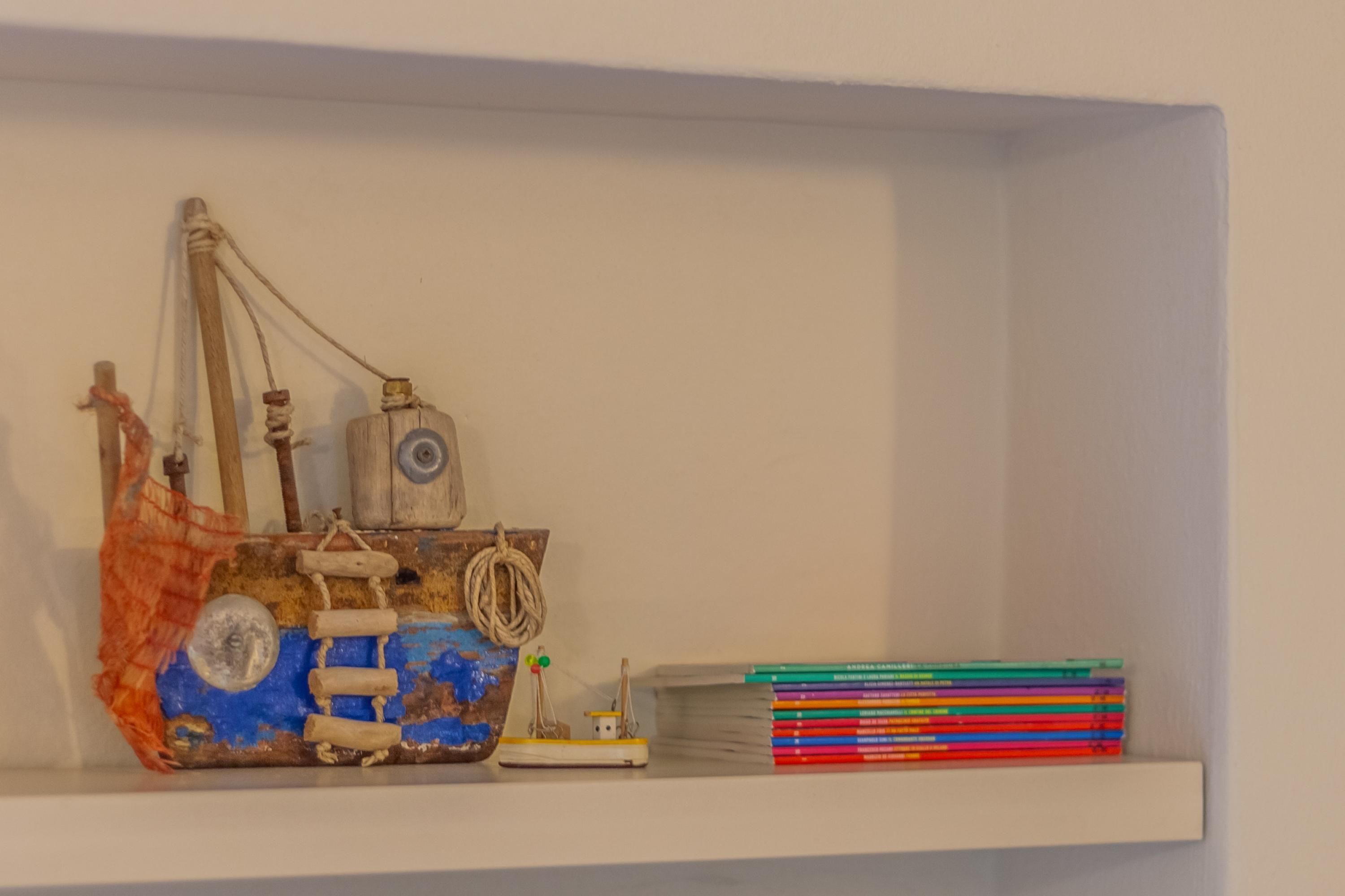 Un estante con un modelo de barco, un bote pequeño y una pila de libros de colores.