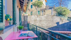 A balcony with a pink table and chairs, a potted plant, and a view of a hillside with buildings. - La Casa di Cora in Perledo (Perledo)