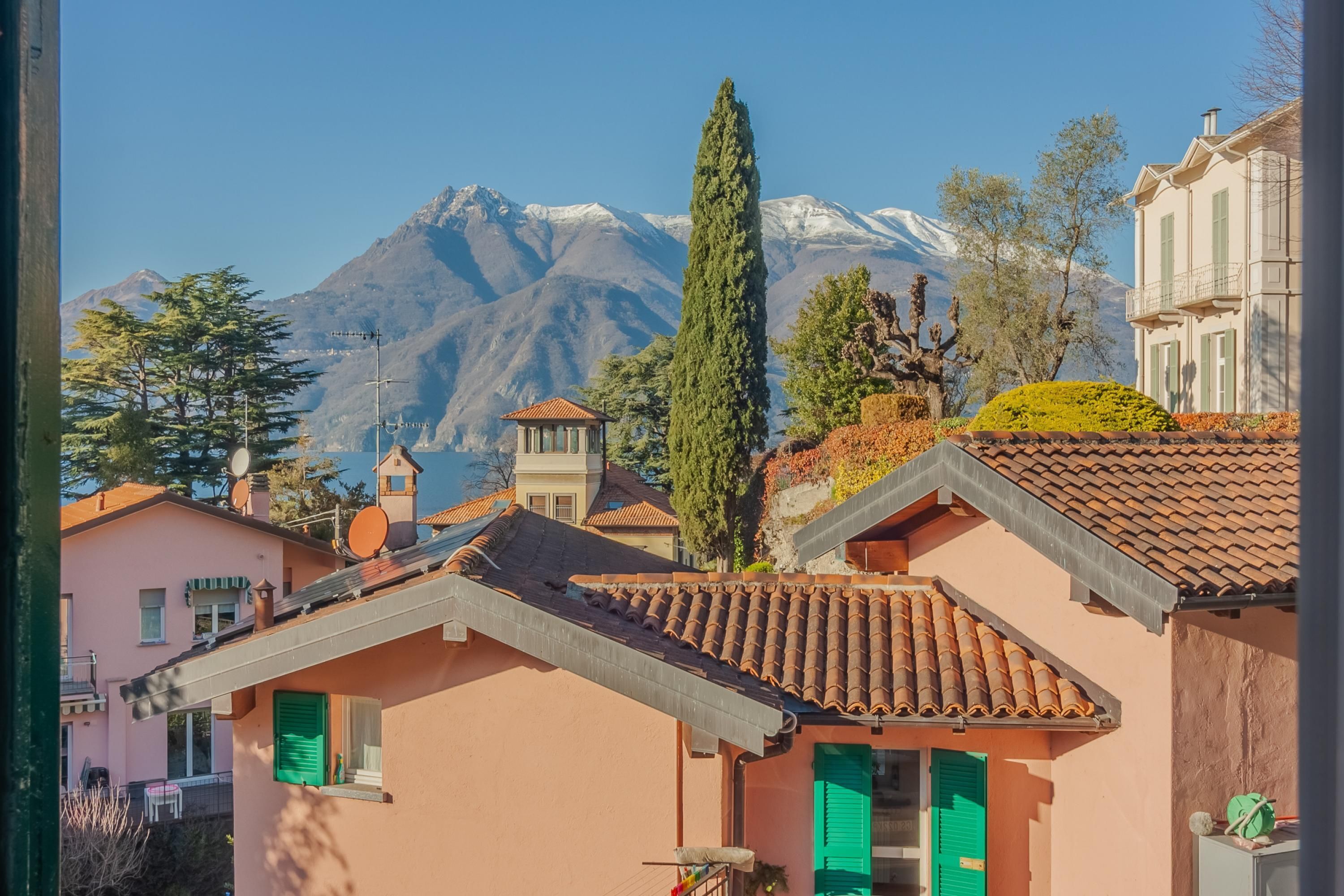 Ein traditionelles Gebäude mit Ziegeldach und grünen Fensterläden, vor einer Berglandschaft und blauem Himmel.