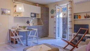 A compact living space with a kitchenette, a dining area, a seating area with a sofa and a chair, and a television. - La Casa di Cora in Perledo (Perledo)