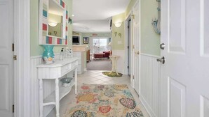 Un pasillo con una consola blanca, un tapete colorido y una puerta que da a una habitación.
