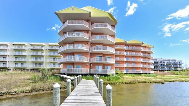 Un hotel frente al agua con varios balcones y un muelle de madera que conduce al edificio.