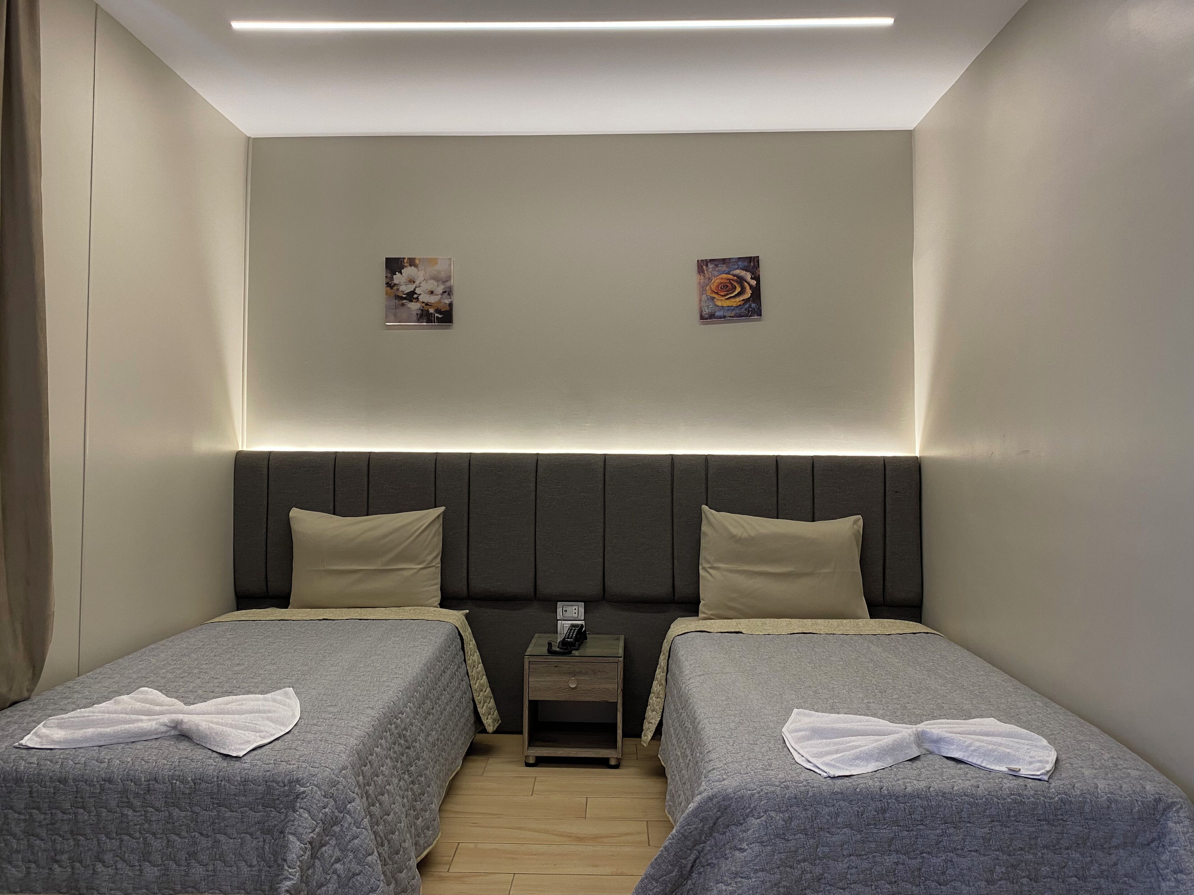 Habitación de hotel con dos camas individuales, una mesita de noche con teléfono y dos cuadros colgados en la pared.