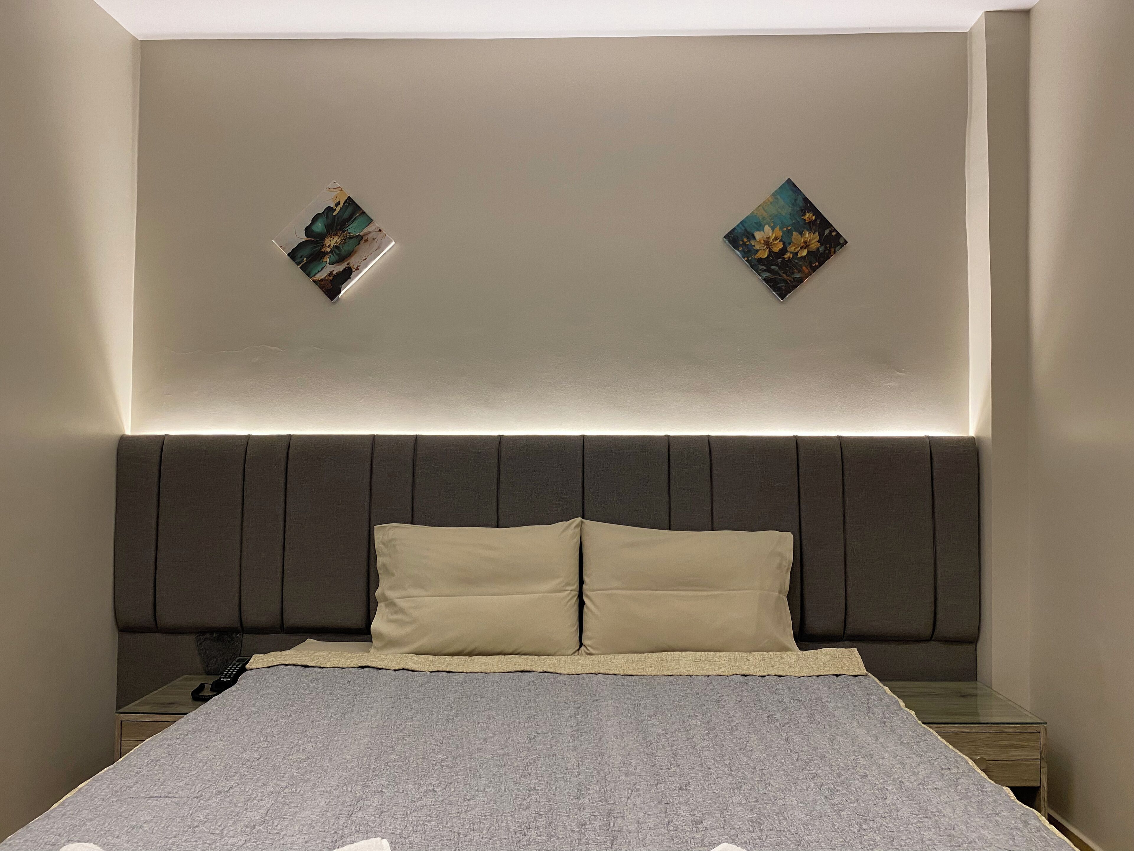 Un dormitorio moderno con una cama grande, dos marcos de cuadros en la pared y una mesita de noche con lámpara.