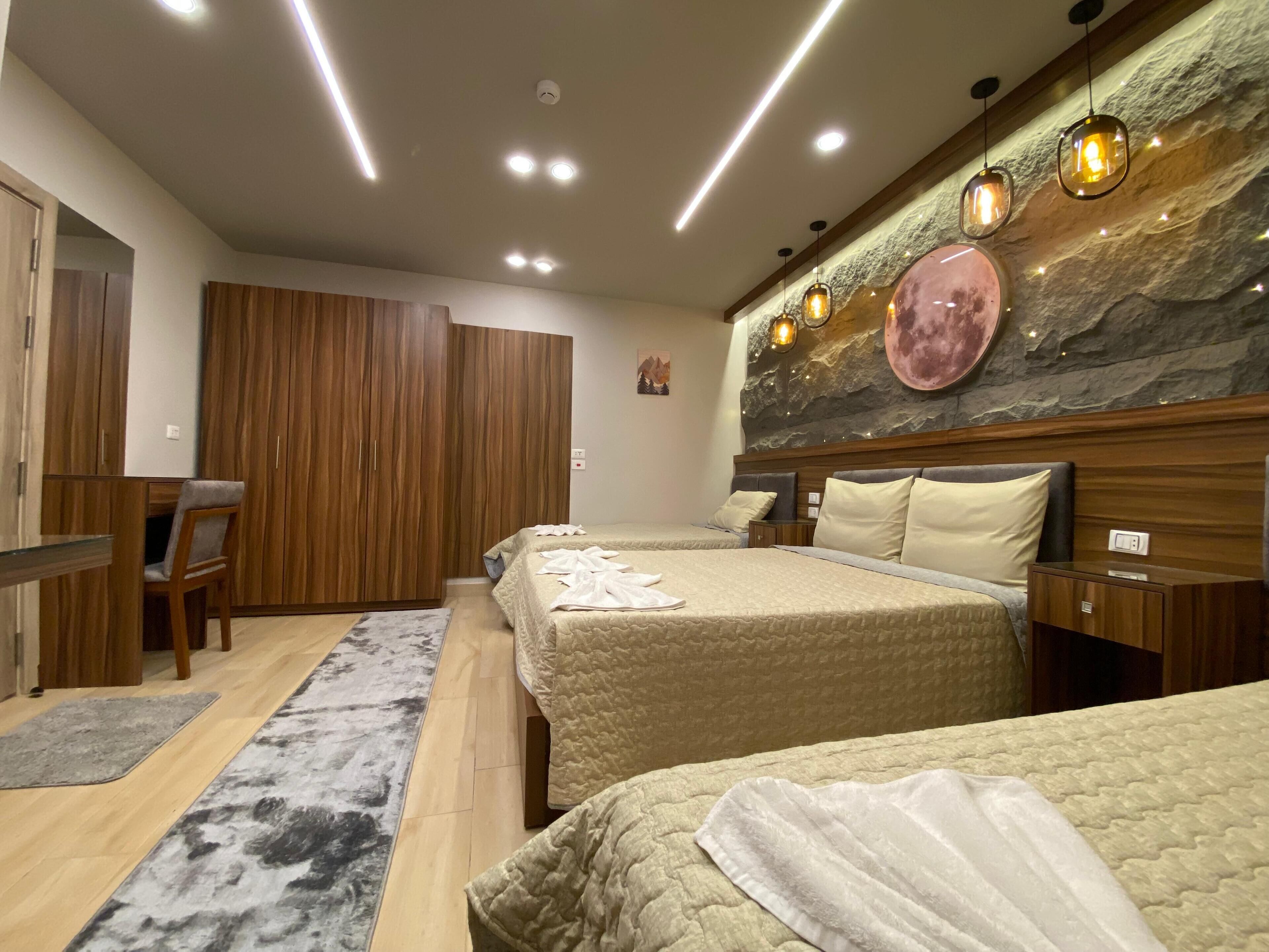 A hotel room with two beds, wooden wardrobe, desk, and a stone wall with a moon decoration.