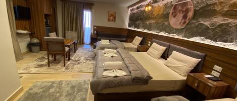A hotel room with a large bed, a smaller bed, a sofa, a desk, and a TV.