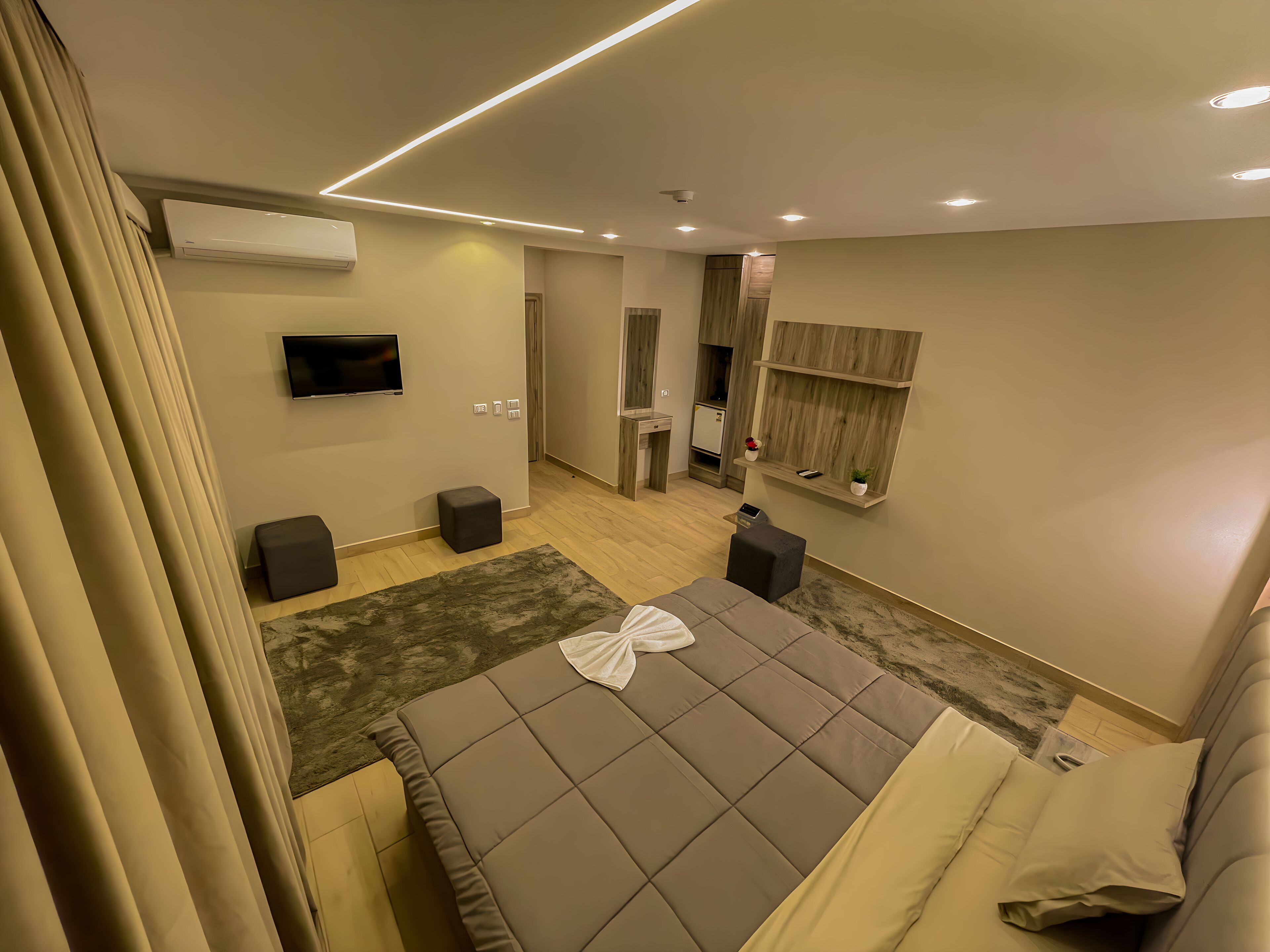 A modern hotel room with a large bed, a flat-screen TV, a small desk, and a built-in wardrobe.