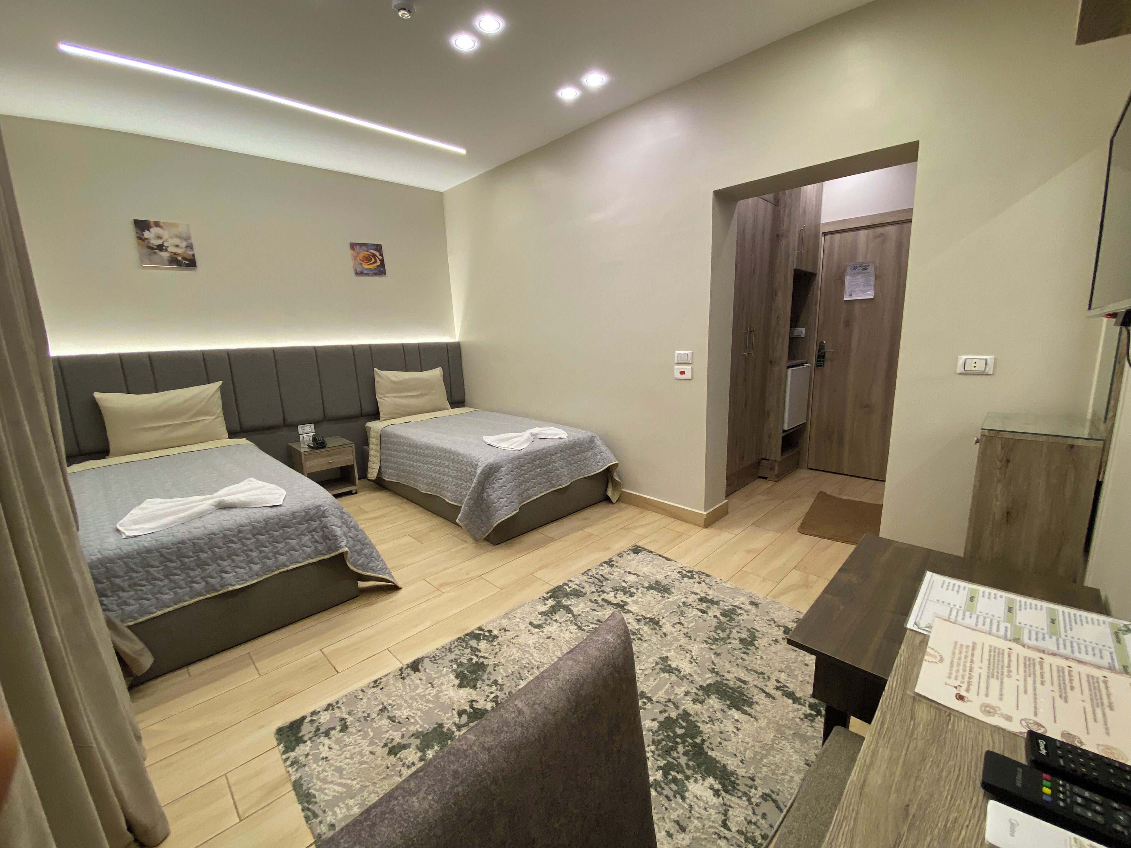 Quarto de hotel com duas camas, uma escrivaninha, uma cadeira, uma mesa pequena e uma porta que dá para o banheiro.