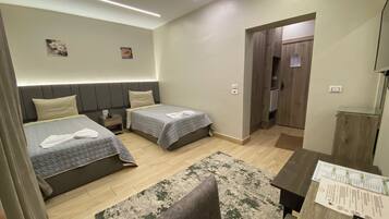 Quarto de hotel com duas camas, uma escrivaninha, uma cadeira, uma mesa pequena e uma porta que dá para o banheiro.
