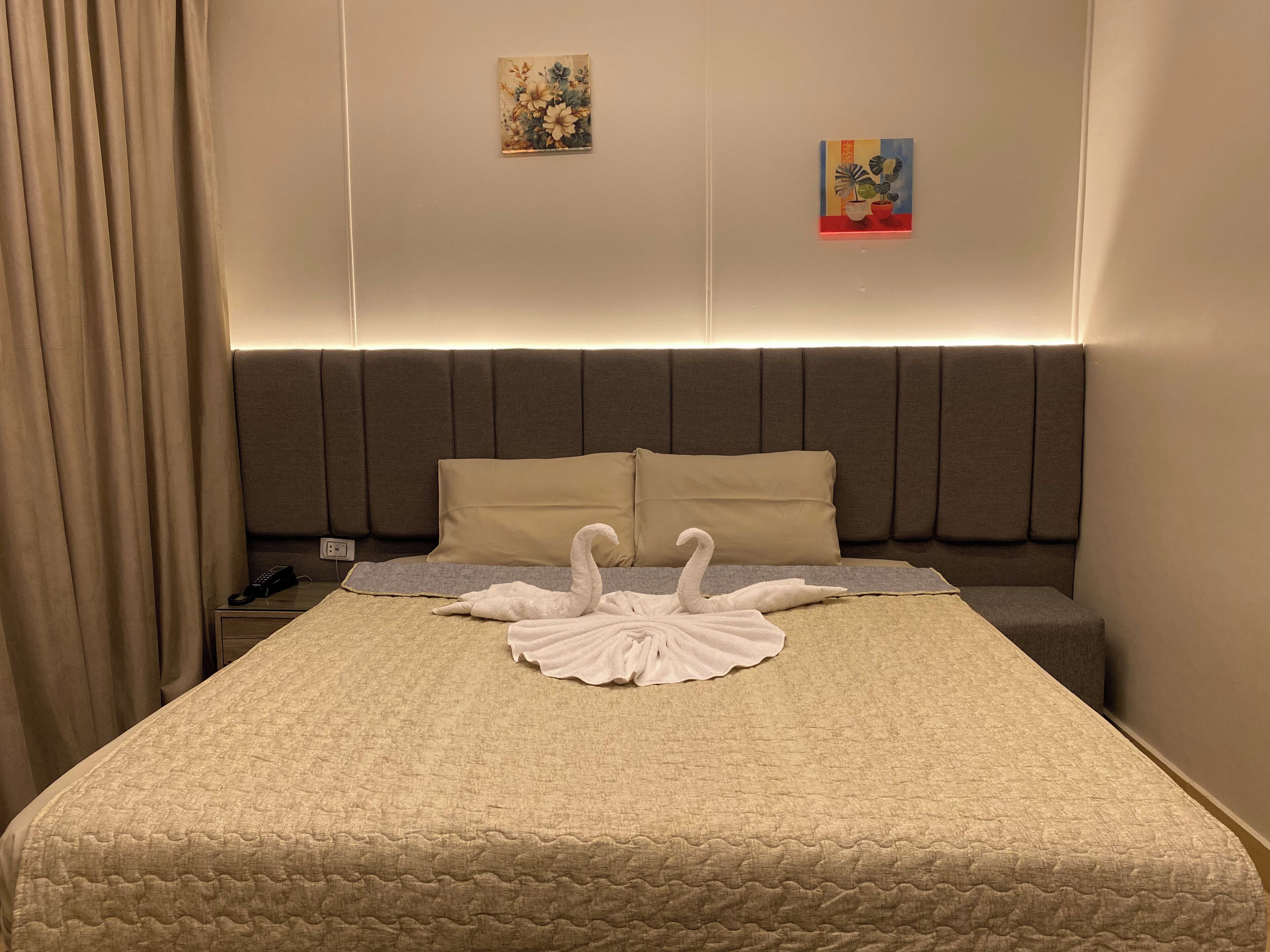 Een hotelkamer met een bed, twee kussens, een nachtkastje met een telefoon en twee aan de muur hangende schilderijen.
