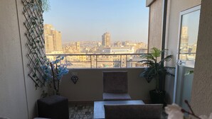 A balcony with a view of a cityscape, featuring a table and two chairs, a potted plant, and a decorative wall panel. - Holy Sheet Plus, Boutique Hotel (Cairo)