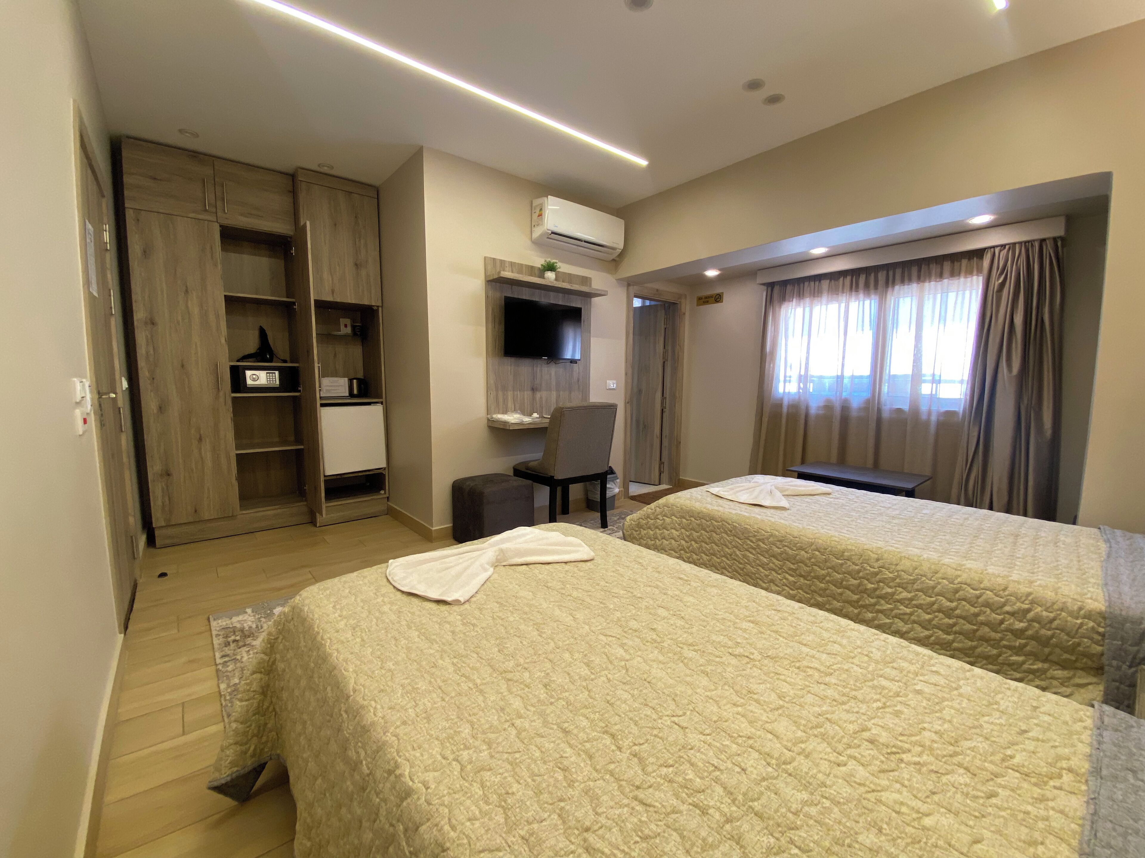 Une chambre d’hôtel avec deux lits, un bureau, une chaise, une armoire et un téléviseur.