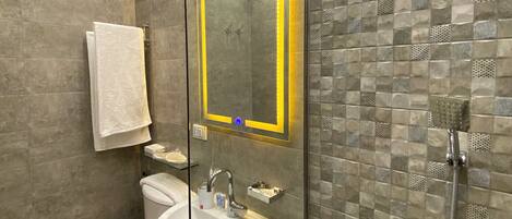 A modern bathroom with a glass-enclosed shower, a toilet, a sink, and a mirror with a yellow frame.
