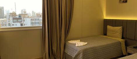 Habitación de hotel con dos camas, una ventana con cortinas, vista a la ciudad y un cuadro pequeño en la pared.