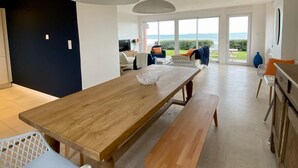 Un'ampia sala da pranzo con tavolo e panche in legno, grandi finestre che si affacciano sull'esterno e un moderno lampadario.