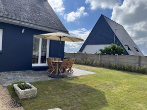Ein Haus mit blauer Fassade, einer Terrasse mit Tisch und Stühlen sowie einem Steinkübel.