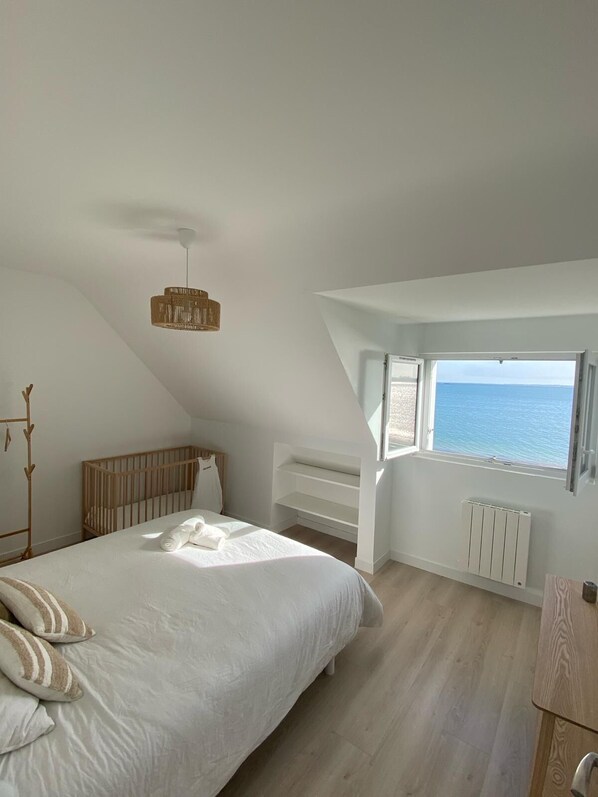 Ein Schlafzimmer mit einem großen Bett, einem Holckrippenbett, einem Heizkörper und Meerblick durch ein Fenster.