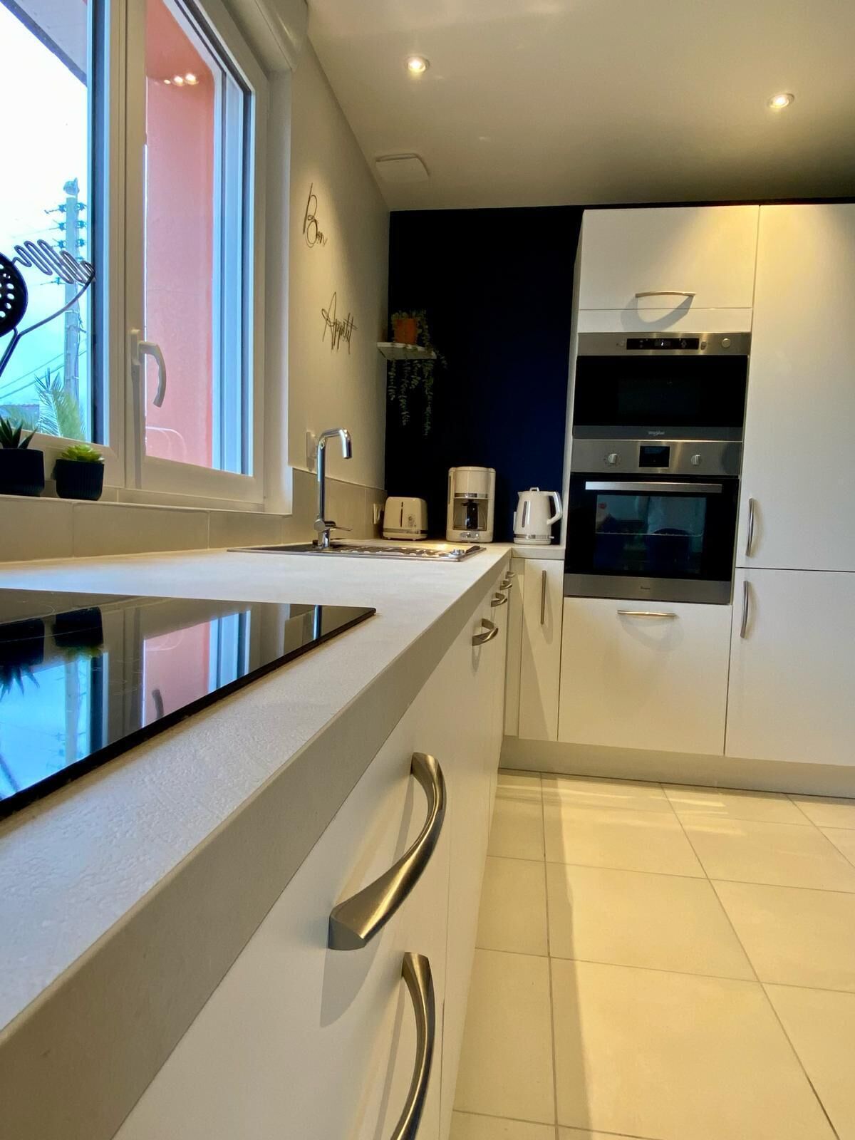 Une cuisine moderne avec des armoires blanches, une hotte de cuisinière en acier inoxydable et une fenêtre donnant sur l’extérieur.