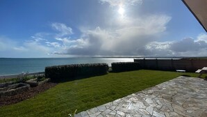 Un'area patio con pavimento in pietra, prato verde e vista sul mare.