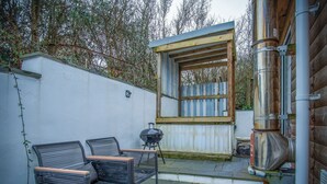 Eine Terrasse mit zwei Metallstühlen, einem Grill und einem Schornstein.