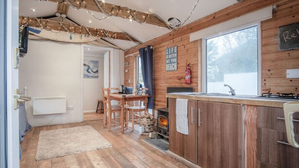 Ein gemütliches Blockhaushaus-Interieur mit Holzvertäfelung, einem Essbereich, einer Küche mit Holzofen und einem großen Fenster.