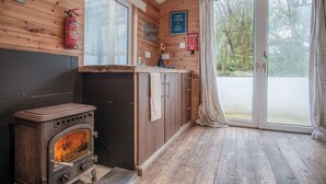 Ein Holzhütten-Interieur mit Holzofen, Holzwänden, einem großen Fenster und einer Tür, die nach draußen führt.