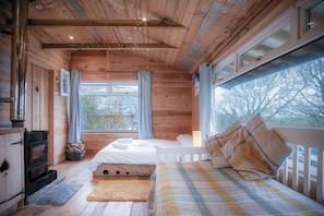 A cozy wooden cabin room with a bed, a fireplace, and large windows. - The Hygge Hut - 1 Bed - Freshwest Beach Retreat (Pembroke)