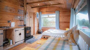 A cozy cabin with a wooden interior, a bed with a plaid blanket, a fireplace, and a window with curtains.