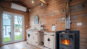 Ein gemütliches Blockhaus-Interieur mit Holzvertäfelung, einem Kaminofen, einer Küchenzeile mit Schränken und einem großen Fenster.