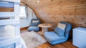 A cozy, sloped-roofed cabin with a bunk bed, two cushioned chairs, a small round table, and a white refrigerator. - The Pod - 1 Bedroom - Freshwest Beach Retreat (Pembroke)
