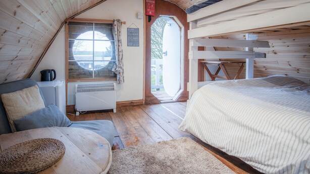 A cozy attic room with a bed, a seating area, and a window. - The Pod - 1 Bedroom - Freshwest Beach Retreat (Pembroke)