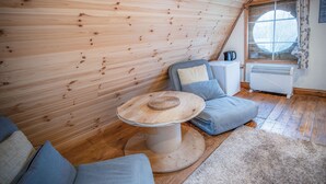 A cozy room with wooden walls, a round table with a woven coaster, a blue sofa with cushions, and a window with curtains. - The Pod - 1 Bedroom - Freshwest Beach Retreat (Pembroke)