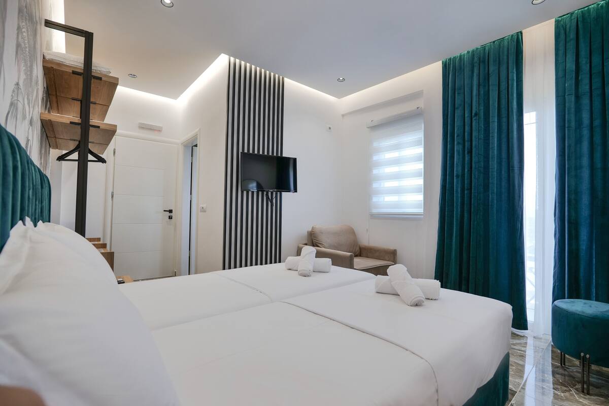 Una habitación de hotel moderna con una cama grande, un televisor de pantalla plana montado en la pared, un sofá y una ventana con cortinas.